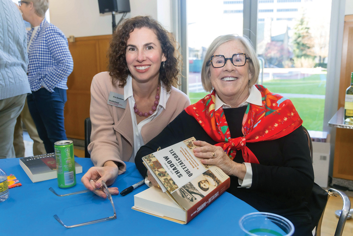 Two women smiling at a book signing event, one holding a book titled "The History of Food."