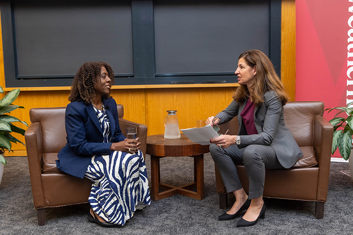 Two women are seated in leather chairs in conversation with each other.