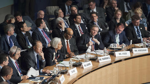Dozens of professionals wearing suits are seated around a table with microphones and name tags.