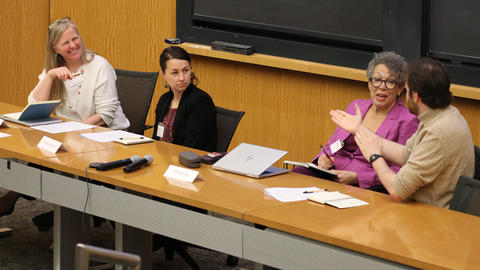 Four professionals are seated at a conference table, talking and listening to each other.