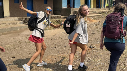 Three students walking down a dirt road, two of whom are looking back to the camera and smiling.
