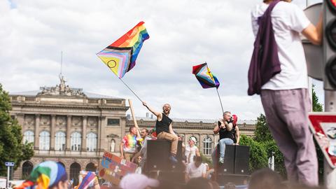 People gathered together, hanging on stoplights and sitting on amplifiers, waving pride flags with joy.