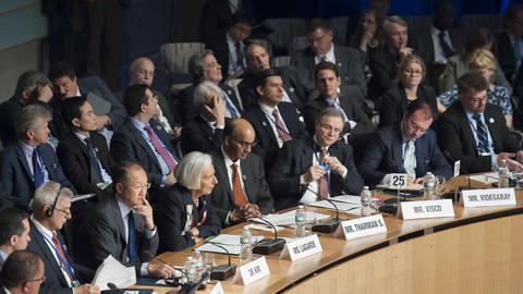 Dozens of people in suits seated around a circular conference table at an IMF meeting.