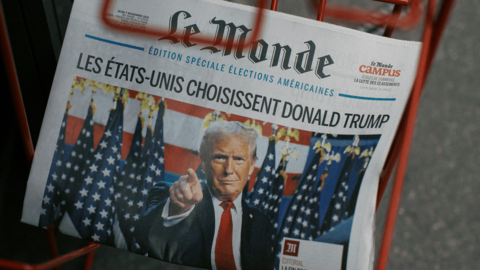 The front page of the French newspaper Le Monde from November 7, 2024 with an image of Donald Trump pointing outward with the headline, “Les États-Unis choisissent Donald Trump” sits in a red newspaper rack.