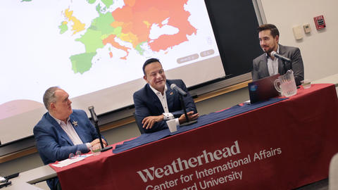Three men sit at a table with microphones in front of a projected map of Europe, at a Weatherhead Center for International Affairs event at Harvard University.