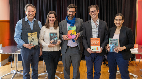 Five professionals stand next to each other, each holding their own book and smiling.