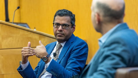 Atul Gawande, gesturing with his hands, speaks in conversation with Erez Manela in a wood paneled room.