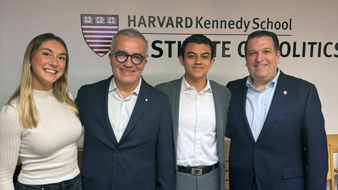 Four people stand side by side, smiling, in front of a wall with the Harvard Kennedy School Institute of Politics logo.