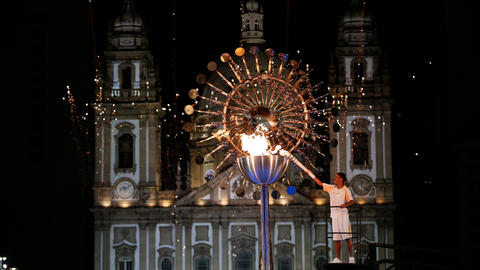Man lights the Olympic torch at night, in front of a majestic white castle. 