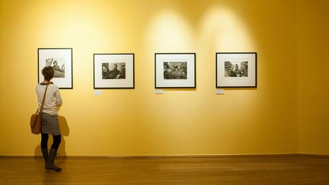 A woman stands in a yellow room, looking at a wall with four black and white photographs on display. 