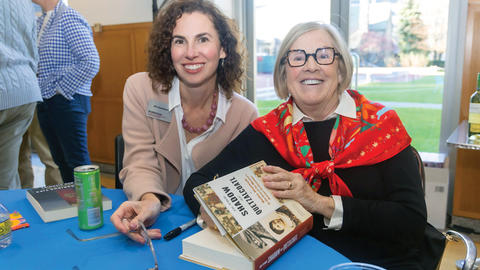 Two women smiling at a book signing event, one holding a book titled "The History of Food."