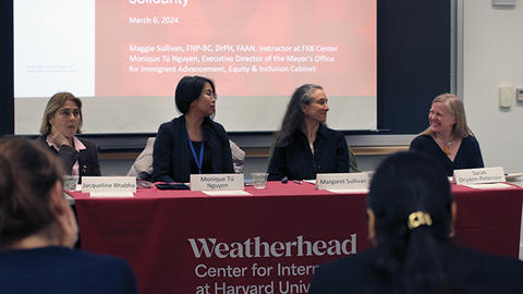 Panel discussion with four women speakers seated at a table, facing an audience, with a Weatherhead Center banner.