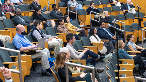 The audience is seated in wooden chairs facing the speaker.