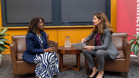Two women are seated in leather chairs in conversation with each other.