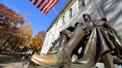 The John Harvard statue on a bright sunny day in Harvard Yard