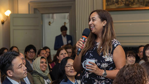 An affiliate stands up in a room of seated people and introduces herself with a microphone.