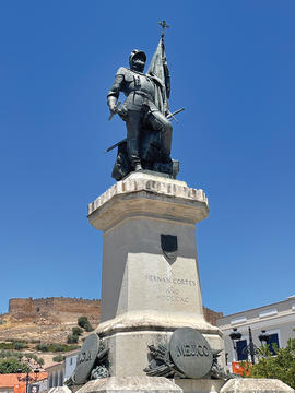 Statue of Hernan Cortes depicting him clad in armor and holding a flag and cross