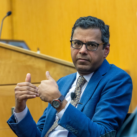Atul Gawande, gesturing with his hands, speaks in conversation with Erez Manela in a wood paneled room.