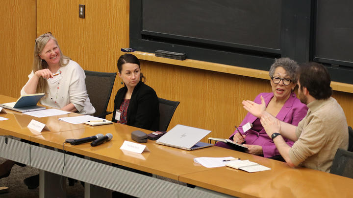 Four professionals seated at a conference table, talking and listening to each other.