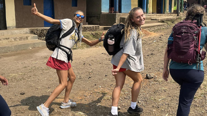 Three students walking down a dirt road, two of whom are looking back to the camera and smiling.