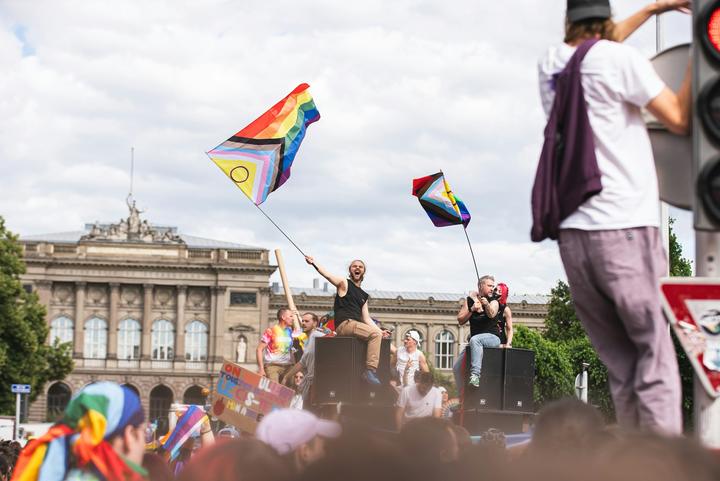 People gathered together, hanging on stoplights and sitting on amplifiers, waving pride flags with joy.