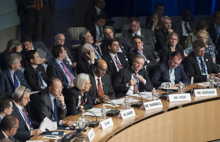 Dozens of people in suits seated around a circular conference table at an IMF meeting.