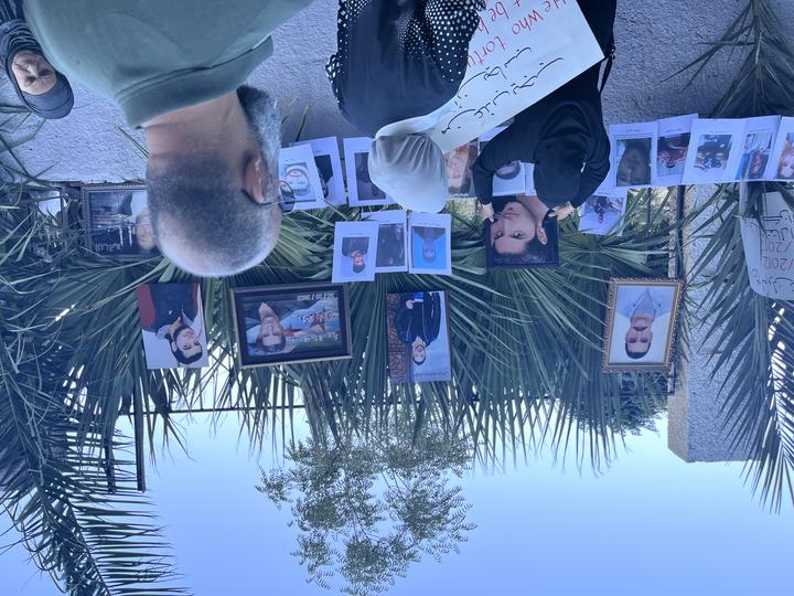 A woman in black hijab hangs a photo of her martyred son on a memorial wall filled with photos.
