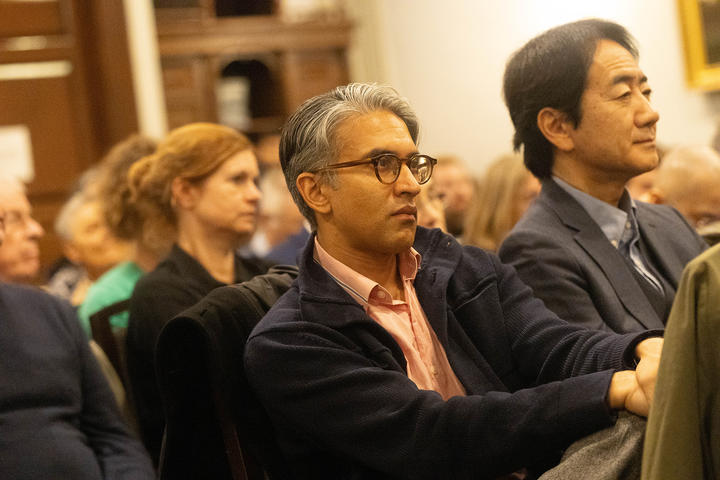 Audience members sit attentively in a lecture hall, focusing on a speaker out of frame.