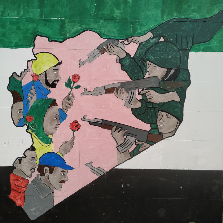 A mural depicts soldiers aiming rifles at civilians holding red roses inside an outline of Syria, with green, white, and black colors in the background.