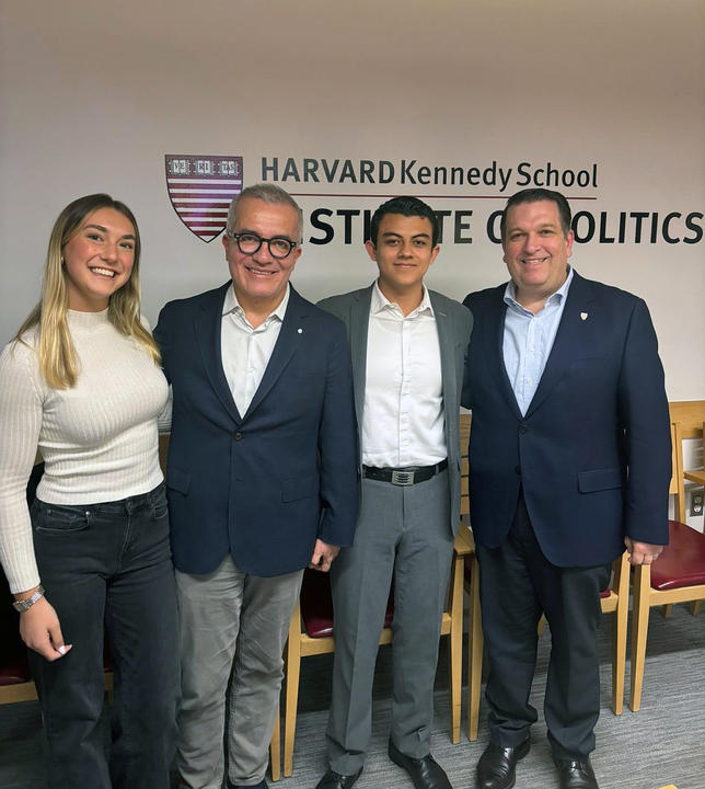Four people stand side by side, smiling, in front of a wall with the Harvard Kennedy School Institute of Politics logo.