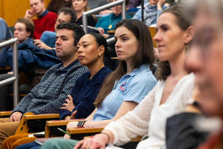 A group of adults sit in an auditorium, attentively listening to a presentation or lecture.