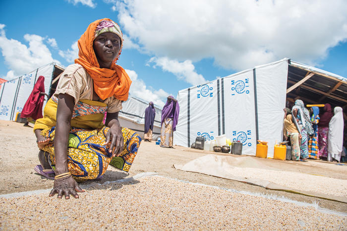 Internally displaced woman kneeling and touching the ground in front of a Nigerian IDP camp