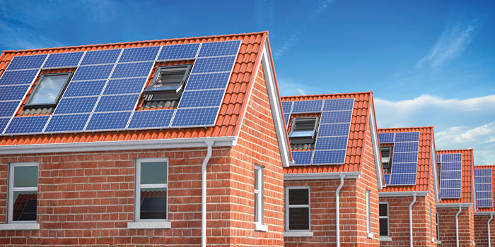 Row of brick houses with solar panels on the roofs under a blue sky.