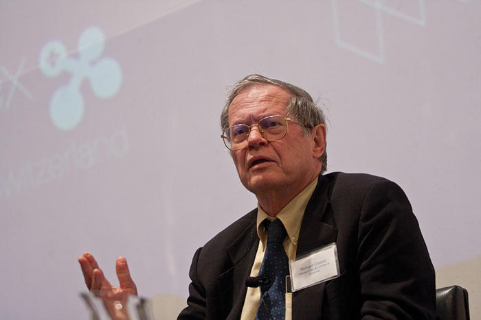Richard Cooper speaks on a panel against a large computer screen