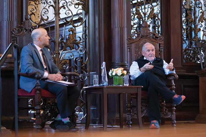 Erez Manela and Larry Brilliant sitting in chairs, talking, at the front of Memorial Churh