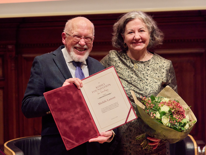 Michele Lamont standing and smiling while holding flowers and receiving the award from another person.