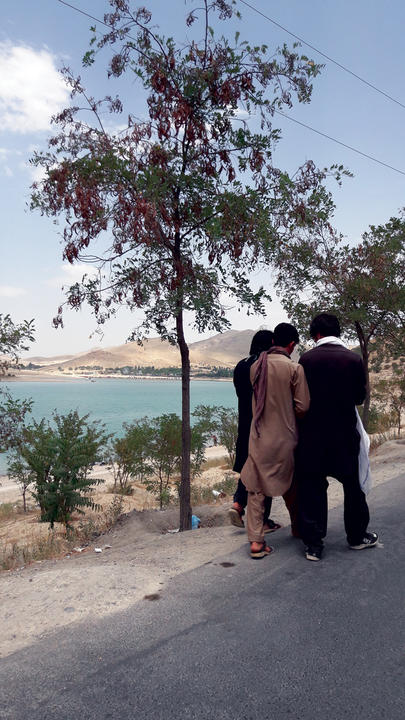 A group of 3 friends walking down the road next to a small body of water