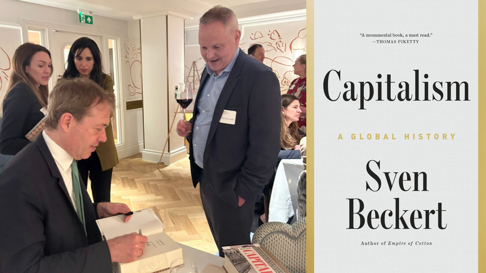 Two-image collage of book cover and a photo of a man in a suit signing a book at a table while another man holding a wine glass stands nearby and people converse in the background at an indoor event.