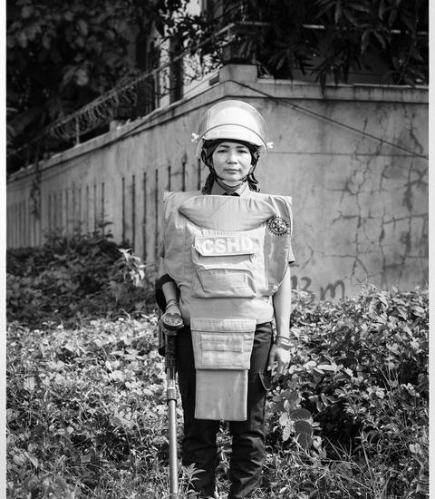 Young woman, standing in a field of weeds and in front of a concrete structure, wears engingeering gear. 