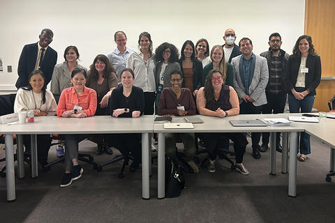 Group photo of about 20 professionals seated and standing behind a conference table.
