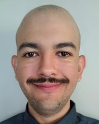 Man with no hair and a mustache is smiling against a blue wall.