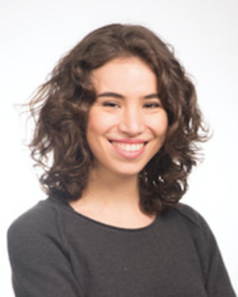 Woman with medium brown hair wearing a black long sleeve shirt folding her arms and smiling.