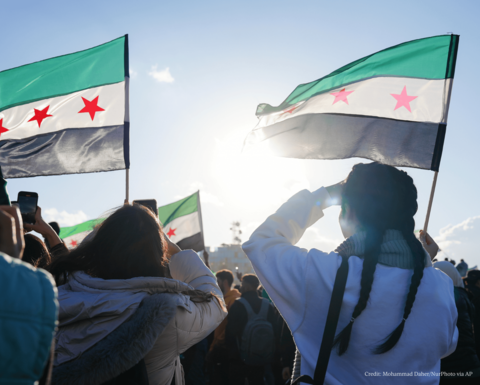 A group of people waving Syrian flags staring into the sun.