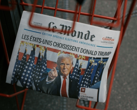 The front page of the French newspaper Le Monde from November 7, 2024 with an image of Donald Trump pointing outward with the headline, “Les États-Unis choisissent Donald Trump” sits in a red newspaper rack.