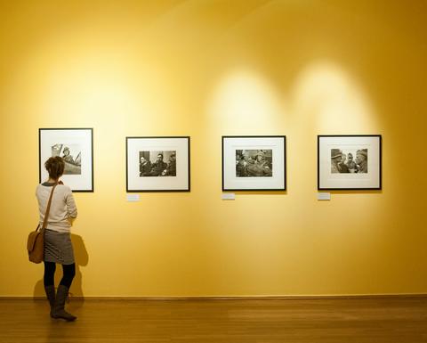 A woman stands in a yellow room, looking at a wall with four black and white photographs on display. 