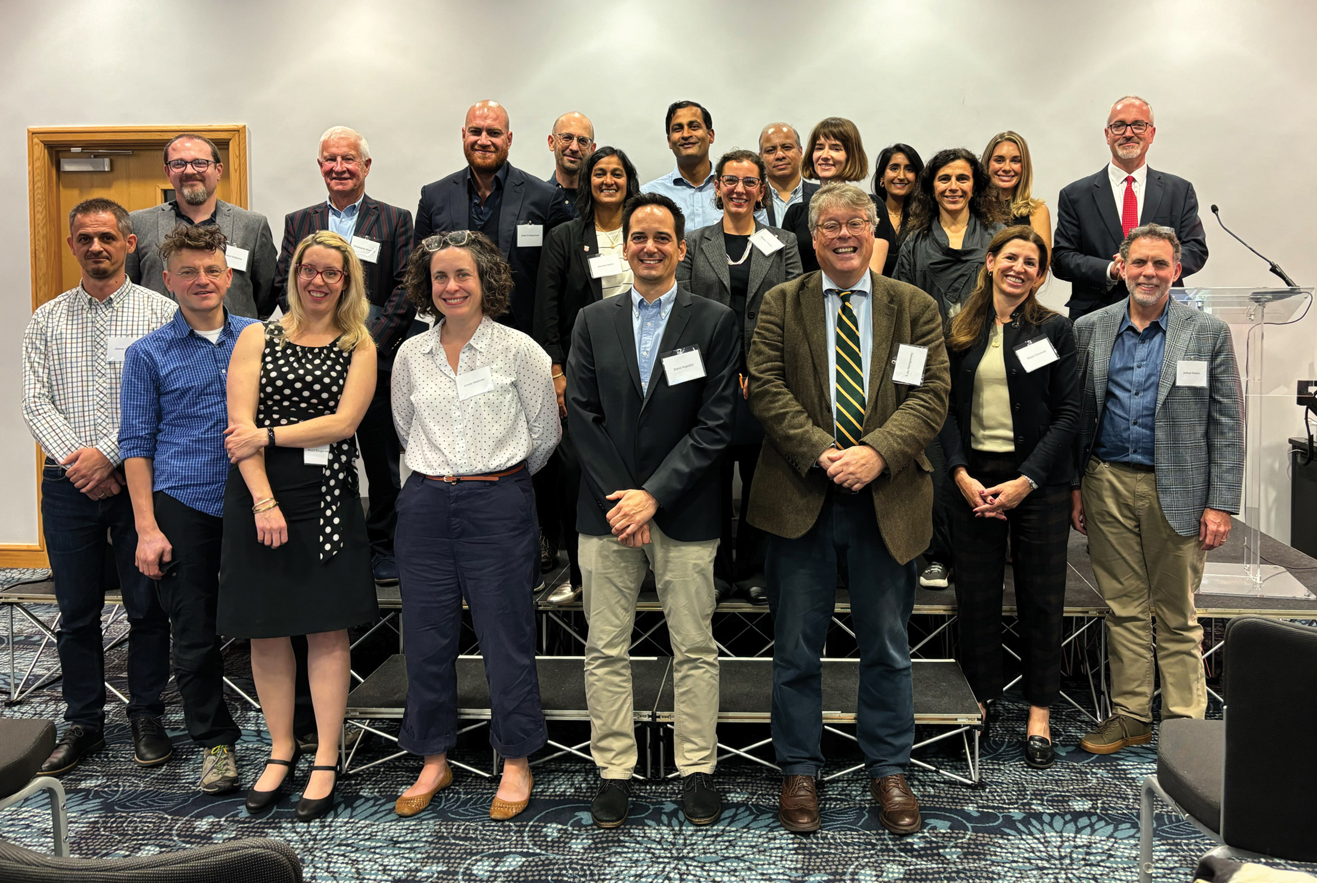 A group of people standing in rows on a platform, posing for a group photo in a conference setting.